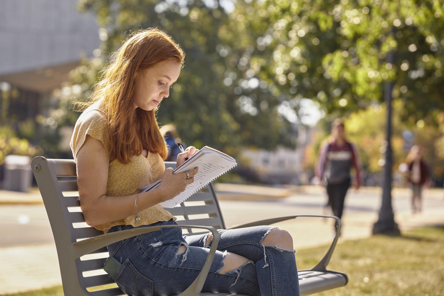 A <a href='http://same.humidifierfinder.com'>博彩网址大全</a> student reads on a bench along Campus Drive.